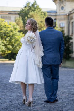 Düğün günü. Gelin ve damat el ele tutuşuyor. Yeni evli çiftimiz fotoşopesyon için dışarıda poz veriyor. Tüm vücut 