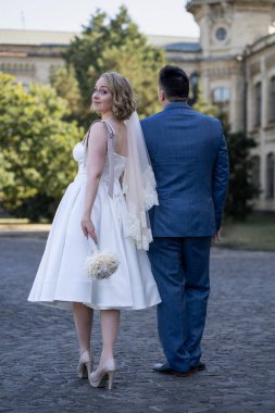 Düğün günü. Gelin ve damat el ele tutuşuyor. Yeni evli çiftimiz fotoşopesyon için dışarıda poz veriyor. Tüm vücut 