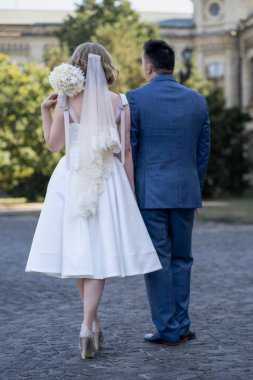 Düğün günü. Gelin ve damat el ele tutuşuyor. Yeni evli çiftimiz fotoşopesyon için dışarıda poz veriyor. Tüm vücut 