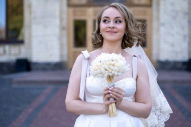 Beyaz gelinlik içinde elinde bir buket çiçekle güzel bir gelinin portresi. Düğün günü. Açık havada gelin fotosferi