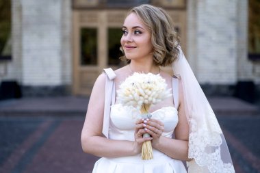 Beyaz gelinlik içinde elinde bir buket çiçekle güzel bir gelinin portresi. Düğün günü. Açık havada gelin fotosferi