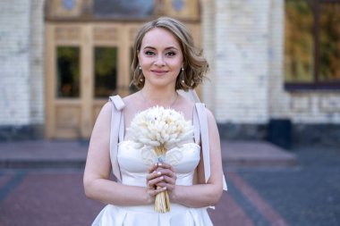 Beyaz gelinlik içinde elinde bir buket çiçekle güzel bir gelinin portresi. Düğün günü. Açık havada gelin fotosferi