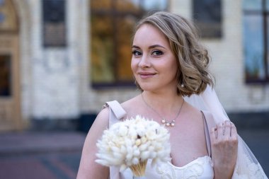 Beyaz gelinlik içinde elinde bir buket çiçekle güzel bir gelinin portresi. Düğün günü. Açık havada gelin fotosferi