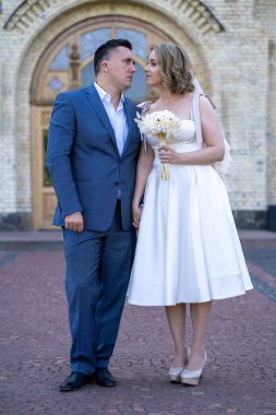 Düğün günü. Gelin ve damat el ele tutuşuyor. Genç ve mutlu bir çift yeni evli fotoşoplar için dışarıda poz veriyor. 