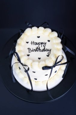 Mutlu yıllar siyah stili. Beyaz doğum günü pastası, kurdeleli Lambeth tarzı. Siyah arka planda Bento keki. Şık bir doğum günü kutlaması.