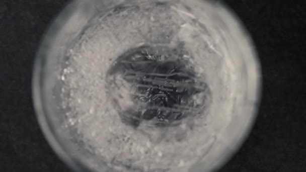 小さなガラスの中の氷のキューブのクローズアップ 透明なガラスの中の氷 透明なガラスの中の水 輝く水の氷のキューブの空気の泡は 水の空気の泡のガラスが浮かぶまで上昇します アイスドリンクアイスキューブ — ストック動画