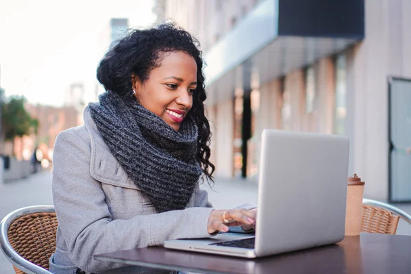 Woman with a laptop happy to work outdoors while having a business online meeting, young lady smiling and working in a coffee terrace . Business concept. High quality photo