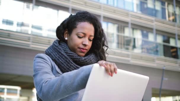 漂亮的黑发女人穿着休闲装 坐在户外用笔记本电脑工作 同时用智能手机聊天 商业概念 高质量的4K镜头 — 图库视频影像