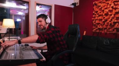 Ses mühendisi profesyonel bir ses stüdyosunda bir şarkıyı eşitlerken eğleniyor, işinden zevk alıyor, haadphone takıyor, bilgisayar ekranına bakıyor ve ses konsoluna dokunuyor.