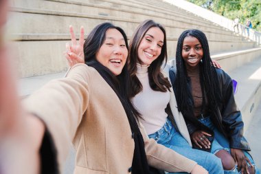 Kameraya gülümseyen bir selfie çeken çok ırklı bir grup genç kadın. Üç farklı kız dışarıda eğleniyor. En iyi arkadaşlar fotoğraf çekiyor. Yüksek kalite fotoğraf