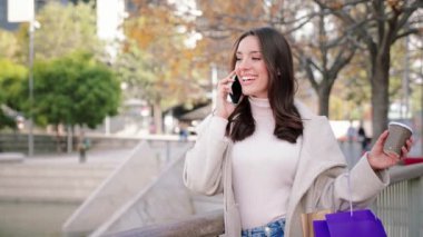 Alışveriş yaptıktan sonra akıllı telefondan arayan genç ve mutlu bir kadın. Dışarda cep telefonuyla konuşan izole bir bayan. Genç kız cep telefonu kullanarak konuşuyor. İletişim konsepti. Yavaş