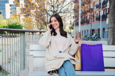 Esmer bir kadın alışveriş yaptıktan sonra bir bankta cep telefonuyla arama yapıyor. Kendini izole edilmiş, gülümseyen ve konuşan genç bir kadın. İletişim konsepti. Yüksek kalite