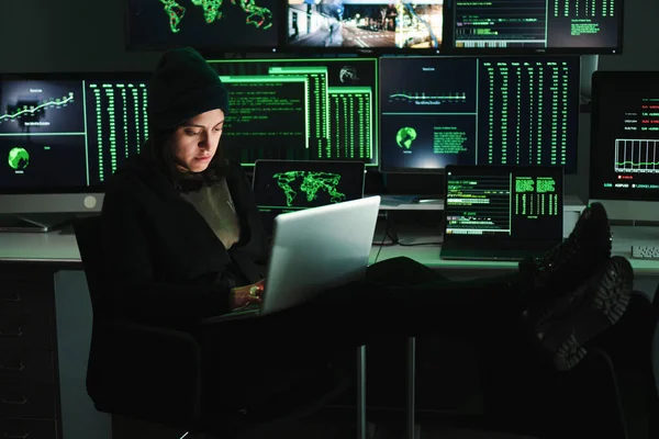Informatic hacker woman typing code on laptop, at background a lot of computer screens with data. Young female programmer doing a firewall attack or phishing with online. Cyber security concept. High