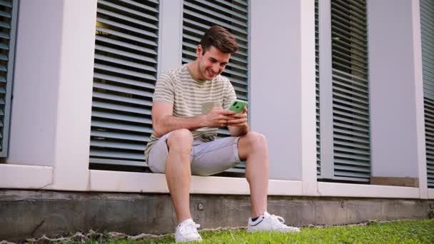 Young Guy Having Fun Playing Game Cellphone Sitting University Campus — 비디오