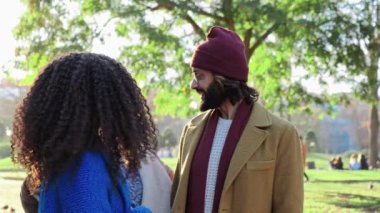 One young multiracial couple talking, then a friend arrives and do greetings and hugs. Group of diverse hipster people embracing toguether. Lifestyle concept. Slow motion. High quality 4k footage