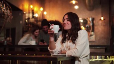 One caucasian happy lady drinking coffee cup in a restaurant or bar. Front view of a young woman smiling and looking at camera after taste a tea indoors. High quality 4k footage