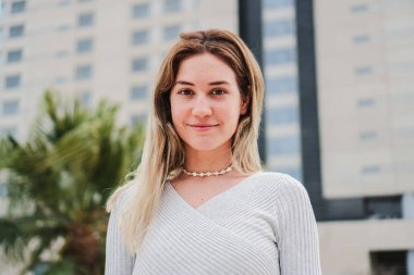 Close up portrait of one happy blonde female smiling looking at camera and touching his hair. Front view of isolated young woman with perfect teeth laughing outdoors. High quality photo