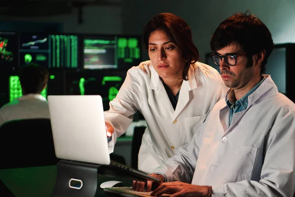 Two concentrated medical scientist with lab coat analyzing a pharmacy test with a laptop computer. A couple of a medicine doctors working in a biology investigation. Science concept. High quality