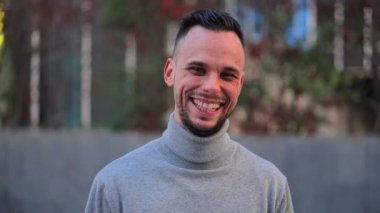 Close up portrait of one handsome business happy young man smiling looking at camera standing outdoors. Front view of isolated cheerful caucasian male face. Slow motion. High quality 4k footage