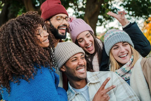 Close up portrait of a group of young people faces, smiling and having fun together. Multiracial happy friends with hats, coats and autumnal clothes enjoying a weekend day. Lifestyle concept. High