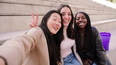 Happy group of multiracial young women taking a selfie portrait smiling at camera. Three diverse girls having fun outdoors. Best friends taking a photo. High quality 4k footage