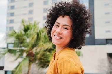 Head shoot portrait of hispanic young woman with curly hair and white teeth lsmiling ooking at camera with carefree attitude. Lifestyle concept. High quality photo