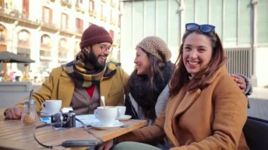 Group of happy friends taking a break drinking a coffee cup in a restaurant terrace, having fun and looking at camera outdoors. Three tourist sitting outside of the bar smiling. . High quality photo