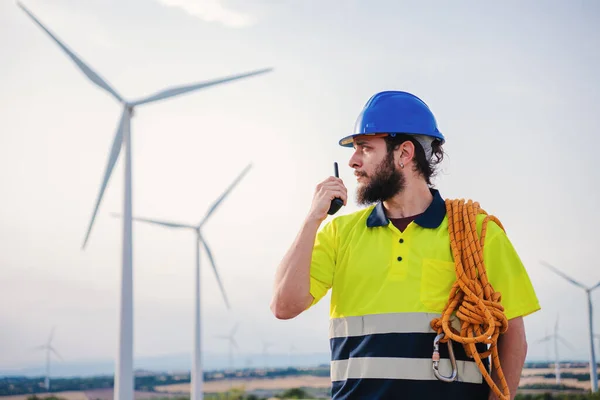 Renewable energy engineer or windmill turbine technician working and talking by walkie talkie, wearing a helmet and professional security clothes. Wind energy concept. High quality photo
