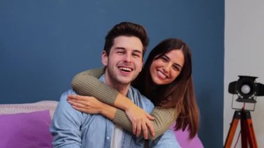 Close up portrait of happy caucasian young couple hugging and smiling together in a couch at home. Beautiful brunette wife embracing her husband resting in a sofa indoors. High quality photo
