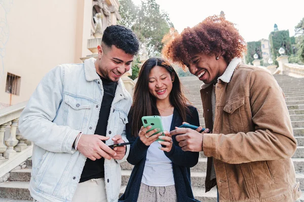 携帯電話を使用してソーシャルメディアアプリで面白いビデオを見ている多人種のティーンエイジャーのグループ 3人の若い友人がコンテンツを共有し スマートフォンと一緒に楽しい時間を過ごしています — ストック写真