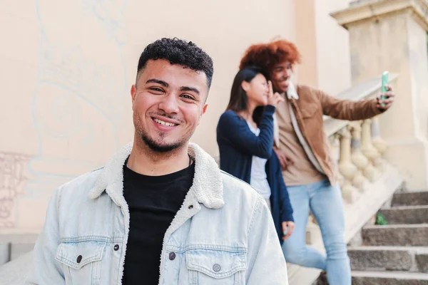 Arka planda gülümseyen ve ayakta duran genç bir Arap 'ın ön görüntüsü. İki çok ırklı arkadaşı birlikte selfie portresi çekiyorlar. Kameraya bakan mutlu bir genç. Yüksek