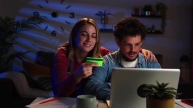 Genç, beyaz, evli bir çift internetten alışveriş yapıyor ve evde kredi kartıyla ödüyor. Mutlu karı koca gülümsüyor. İnternetten e-ticaret siparişi veriyor. Gece yarısı bilgisayar kullanıyor.