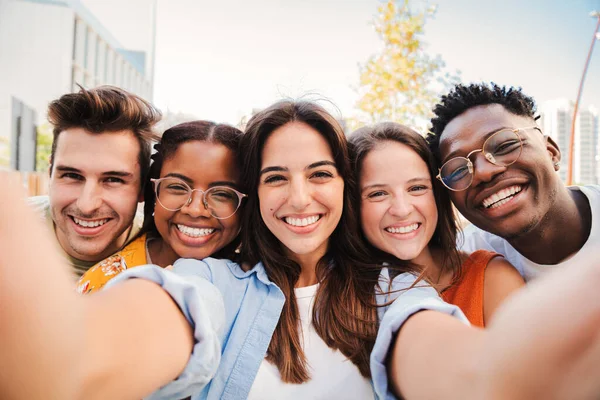 Bir grup mutlu, çok kültürlü genç gülümseyip bir öğrenci toplantısında selfie çektirirken eğleniyor. Çok ırklı beş genç arkadaş gülüyor ve akıllı telefonuyla fotoğraf çekiyor. Yüksek