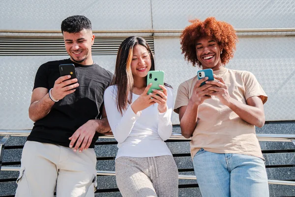 Snsで写真をシェアするために一緒にスマートフォンを使っている多人種の幸せな10代の若者のグループ 外に立っている携帯電話を使用してインターネットで楽しいブラウジングをしている3人の多民族の若い友人 — ストック写真