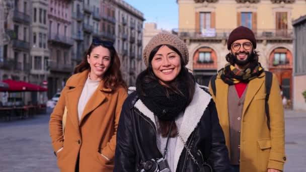 ヨーロッパの街の通りに笑みを浮かべてカメラを見て立っている観光客の友人のグループ 屋外に立つ旅の旅に3つの幸せな旅行者の観光の肖像画 ライフスタイルのコンセプト — ストック動画