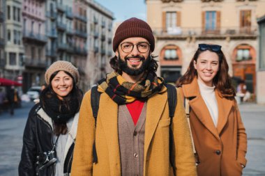 Birlikte gülümseyen ve dışarıda kameraya bakan mutlu gençlerin portresi. Avrupa 'da gezinin tadını çıkaran üç hippinin ön görüntüsü. Ön planda sakallı bir adam