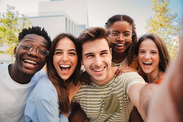 Mutlu çok kültürlü arkadaşlar birlikte selfie çektirirken gülüyorlar. Karışık neşeli genç öğrenciler eğleniyor ve takılıyor. Genç, çok ırklı, neşeli insanlar kameraya ve kaynaşmaya bakıyor. Yüksek