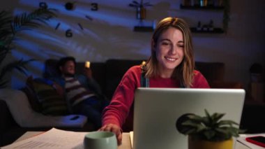 Genç, beyaz, sarışın bir kadın ev ofisinin bilgisayarında geceleri masasında oturuyor. İnternette kablosuz bağlantıyla gezinmek için bilgisayar kullanan mutlu bir bayan girişimci. Yüksek