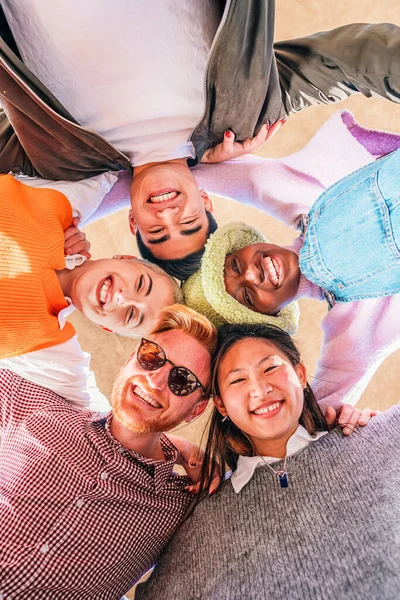 楽しさとカメラを見ている多人種の幸せな若い友人の垂直低角度ビュー 複数の民族の陽気な人々のグループの下の肖像一緒に輪の結合に立って笑顔 — ストック写真