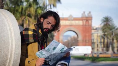 Sakallı bir turist, Barselona 'yı ziyaret eden bir anıt bulmak için harita okuyor. Yetişkin bir gezgin bir rehber arıyor, kameraya bakıyor ve seyahatte geziyor.