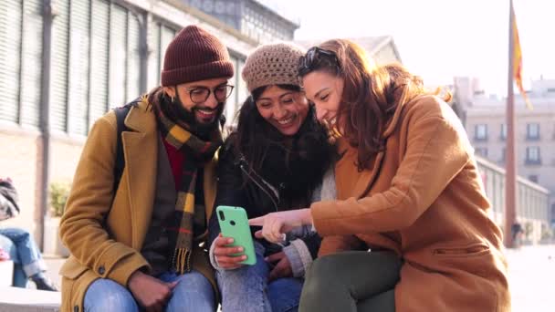 屋外でスマートフォンを使って幸せな若者のグループ 3人の陽気な友人が一緒に笑顔と携帯電話を見て 観光客は携帯電話アプリでインターネットで楽しいブラウジングをしています — ストック動画