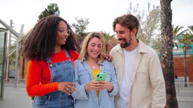 Bir grup çok ırklı arkadaş cep telefonuyla eğleniyorlar sosyal medyada komik videolar izliyorlar, oyunlar oynuyorlar, mesajlar gönderiyorlar. Birlikte telefon kullanarak gülen ve gülen üç genç insan.