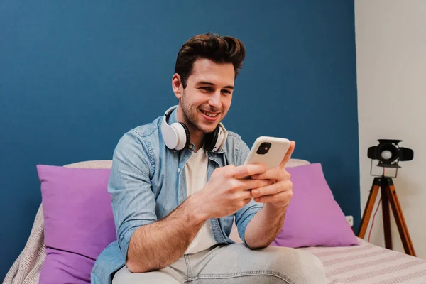 Bir genç cep telefonuyla internette gezinirken eğleniyor. Oturma odasındaki kanepede oturan akıllı telefon kullanan yakışıklı bir genç. Sosyal medya uygulamasında gülümseyen ve paylaşan yakışıklı adam.