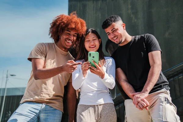 若い多文化のティーンエイジャーは スマートフォンで面白い画像を見ています 3人の笑顔の若い大人の人々が携帯電話アプリでインターネット上で閲覧 幸せな学生が携帯電話を使用してビデオゲームをプレイ — ストック写真