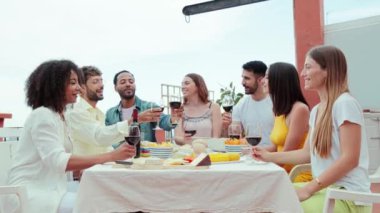 Çatı katındaki bir akşam yemeğinde gülümseyen ve kadeh tokuşturan bir grup yetişkin arkadaş. Genç mutlu insanlar arkadaşça bir toplantıda alkolle kadeh kaldırırken eğleniyorlar. Yüksek