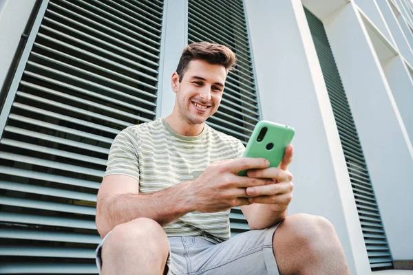 Arkadaşça bir ifadeyle gülümseyen ve dışarıda cep telefonuyla oyun oynarken eğlenen genç bir adam. Sosyal medyayı izlemek için cep telefonu kullanan beyaz tenli bir afet.