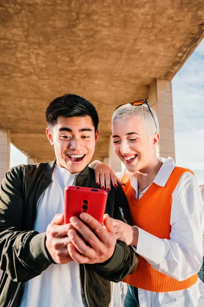 ソーシャルメディアアプリの写真を見るために携帯電話を使用して若いカップルの垂直肖像画 多人種の人々が携帯電話を持って一緒に楽しみます ボーイフレンドとスマートフォンとガールフレンド — ストック写真