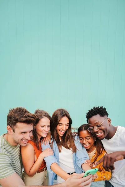 若い友人の多人種グループの垂直肖像画は ティールブルーの壁の背景に彼らの携帯電話のアプリを使用して笑顔 ソーシャルメディアでコンテンツを見るのが楽しい10代の多様な学生 — ストック写真