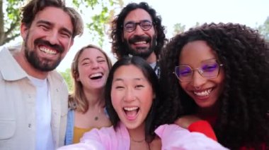 Bir grup neşeli genç arkadaş el sallıyor ve hafta sonundaki sosyal toplantının keyfini çıkarırken kameraya bakıyorlar. Çok ırklı mutlu insanlar partide birlikte gülümseyen bir selfie çekiyorlar.