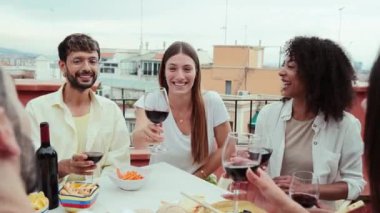 Ağır çekim. Bir grup mutlu arkadaş kırmızı şarap bardaklarını tokuşturup anın tadını çıkarıyor, çatıda aperatif olarak içiyorlar. Gülümseyen gençler birlikte eğlenirken kadeh kaldırıyor, içiyor ve konuşuyor.